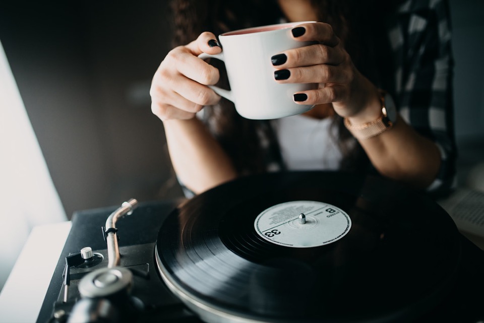 A woman's hands cradling a warm mug while a record plays